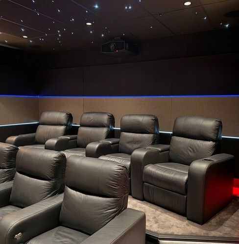 Two rows of black leather cinema recliners beneath a ceiling-mounted projector