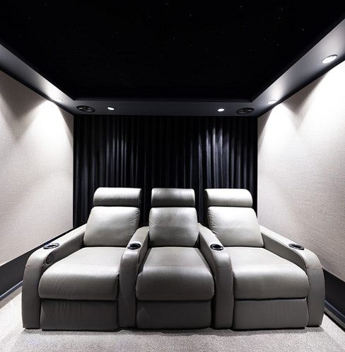 Tres butacas reclinables de cine de color gris bajo un techo con luces de estrellas y focos empotrados