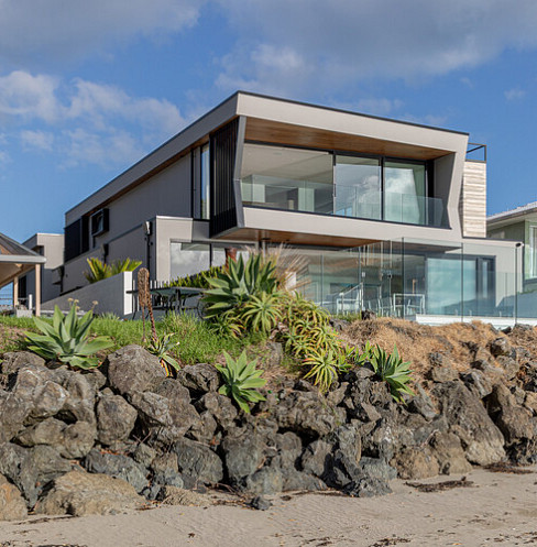 Modern coastal smart home exterior with full-height glazing and landscaped rock garden