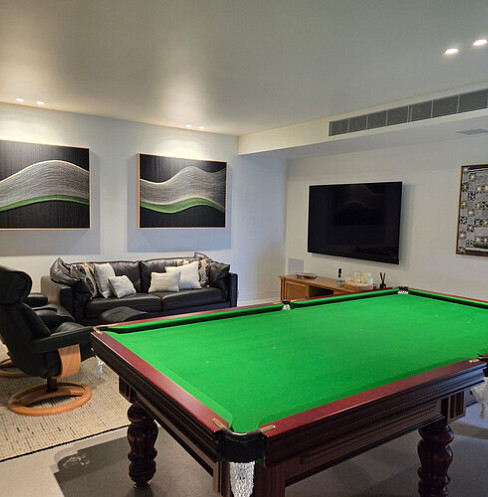 Sala de juegos con televisión montada en la pared, iluminación inteligente y mesa de billar de tamaño estándar