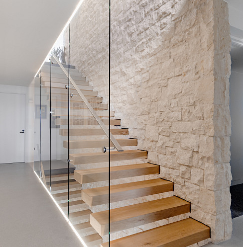 Escalera con paredes de cristal, pasamanos iluminado y pared decorativa de piedra