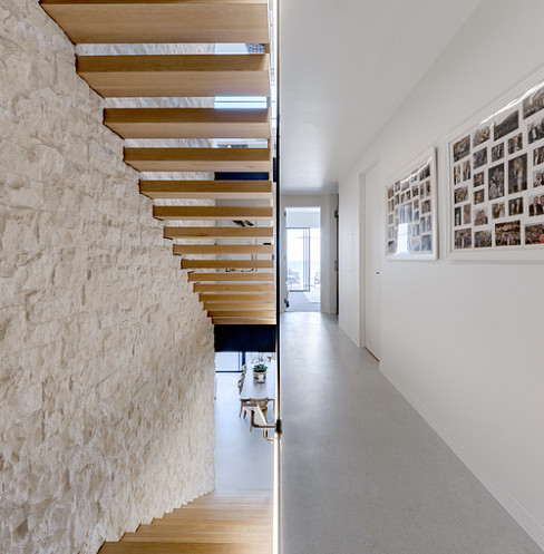 Pasillo minimalista con escalera flotante de madera e iluminación lineal discreta