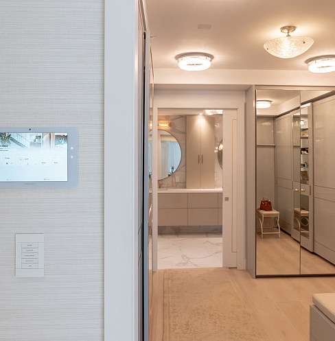 Pantalla táctil Crestron instalada junto a un cuarto de baño luminoso y un vestidor con espejos