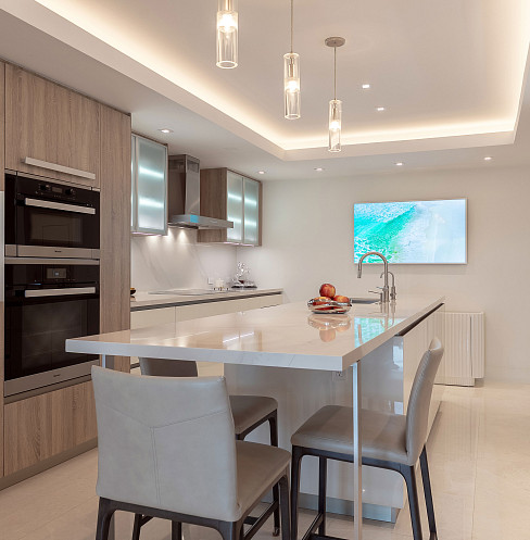 Cocina moderna con iluminación integrada, altavoces en el techo y televisor montado en la pared