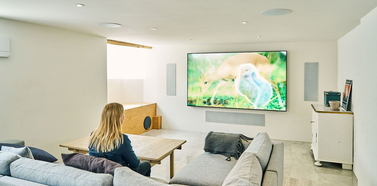 Family watching a wall-mounted TV in a home cinema with discreet DALI architectural speakers