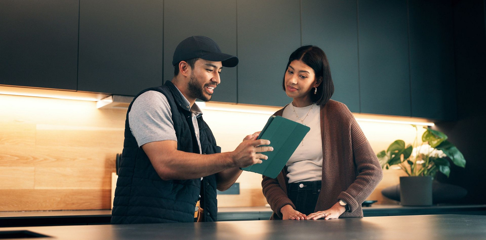 Smart home installer discussing a tablet-based system plan with a homeowner in a kitchen